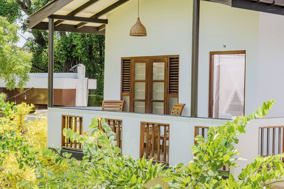 A white building with wooden shutters, a balcony with chairs, and a hanging light fixture.