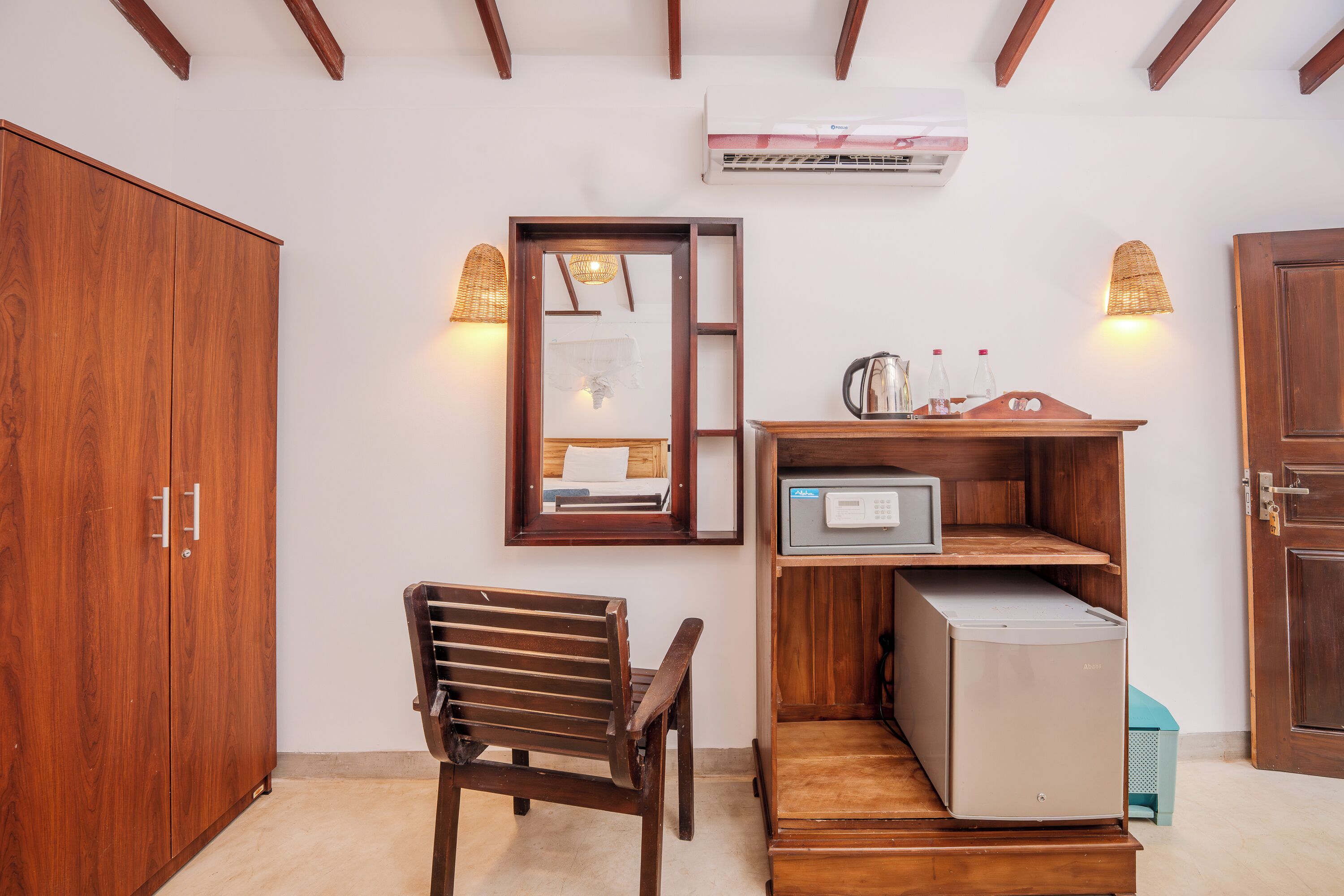 A compact room with a wooden wardrobe, a small wooden chair, a microwave, and a shelf with kitchen items.