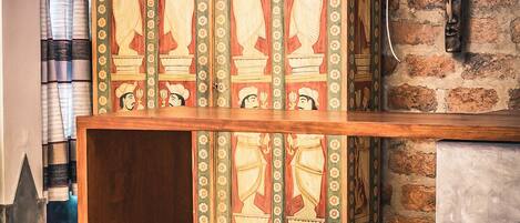 A bar area with a wooden counter and stools, a brick wall, and a decorative cabinet with painted figures.