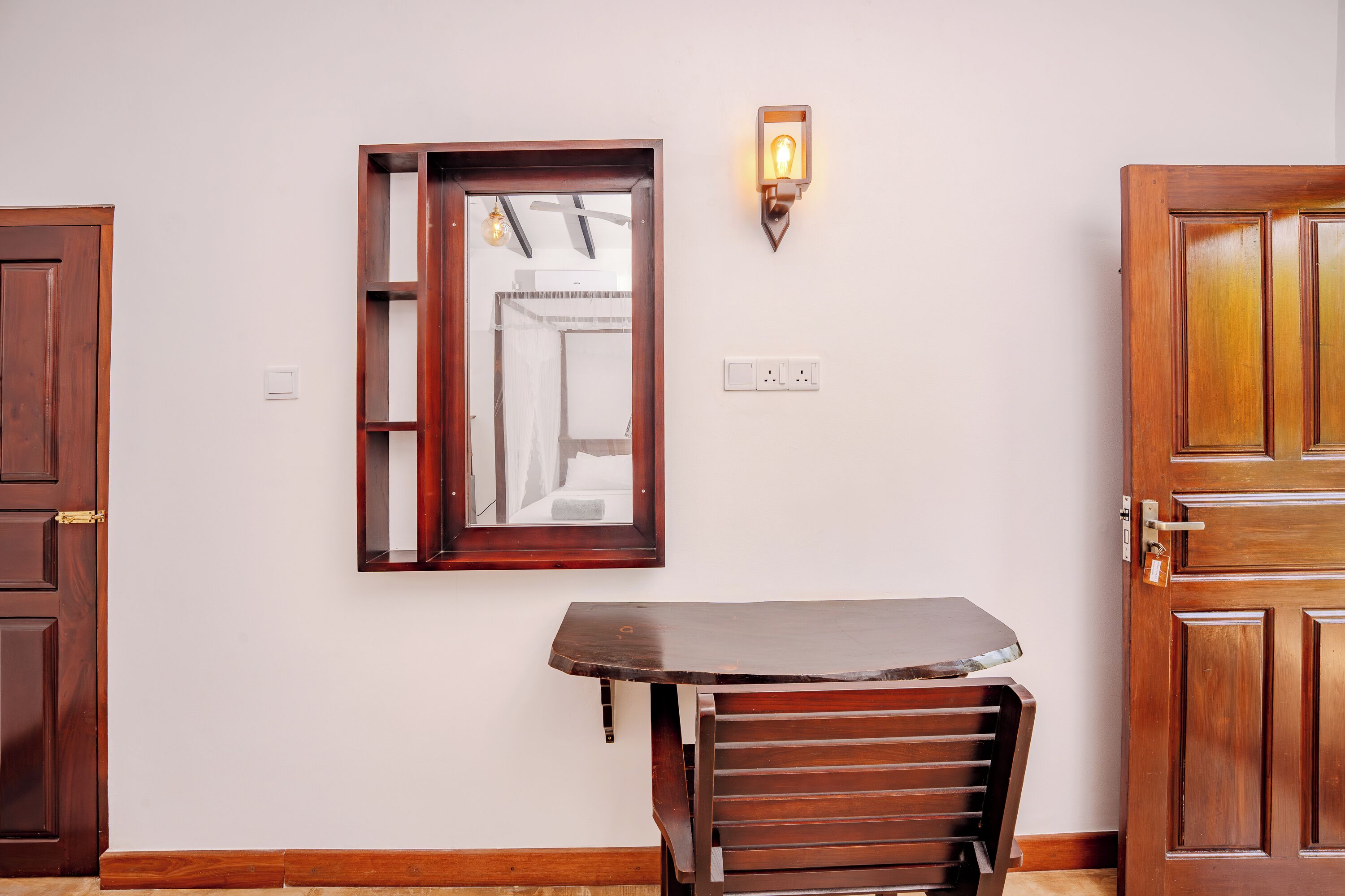 A room with a wooden door, a mirror, a wall-mounted light fixture, and a wooden bench.