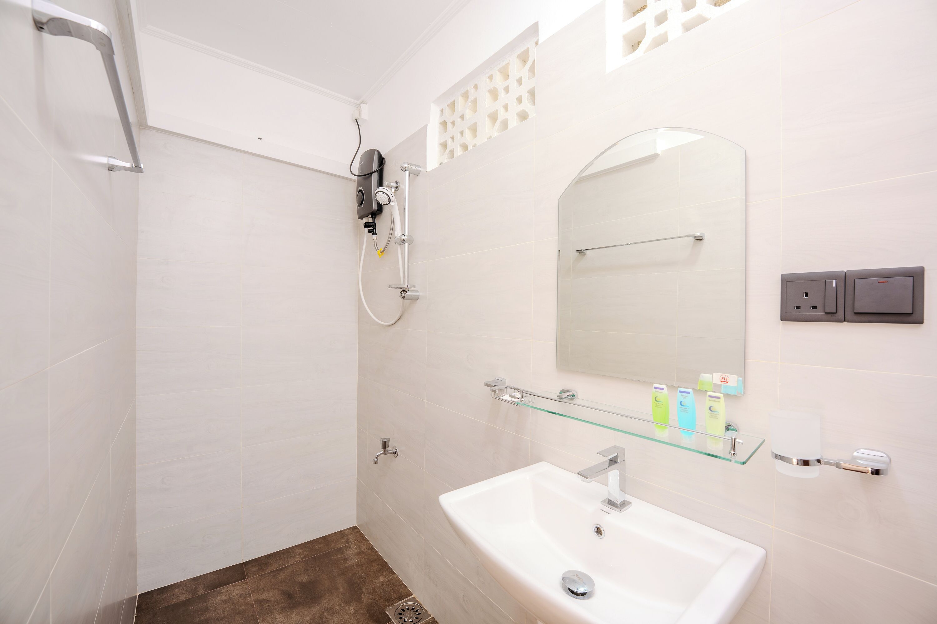 Un baño moderno con ducha, lavamanos y repisa de vidrio con artículos de aseo.