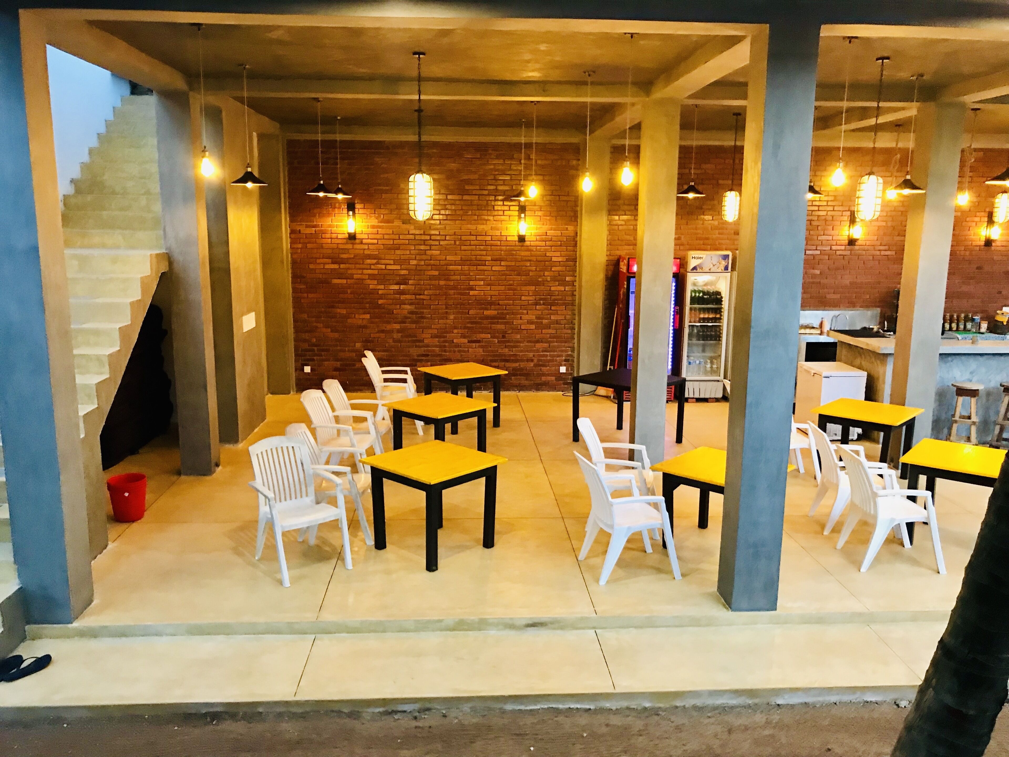 A restaurant with tables and chairs, a brick wall, and hanging lights.
