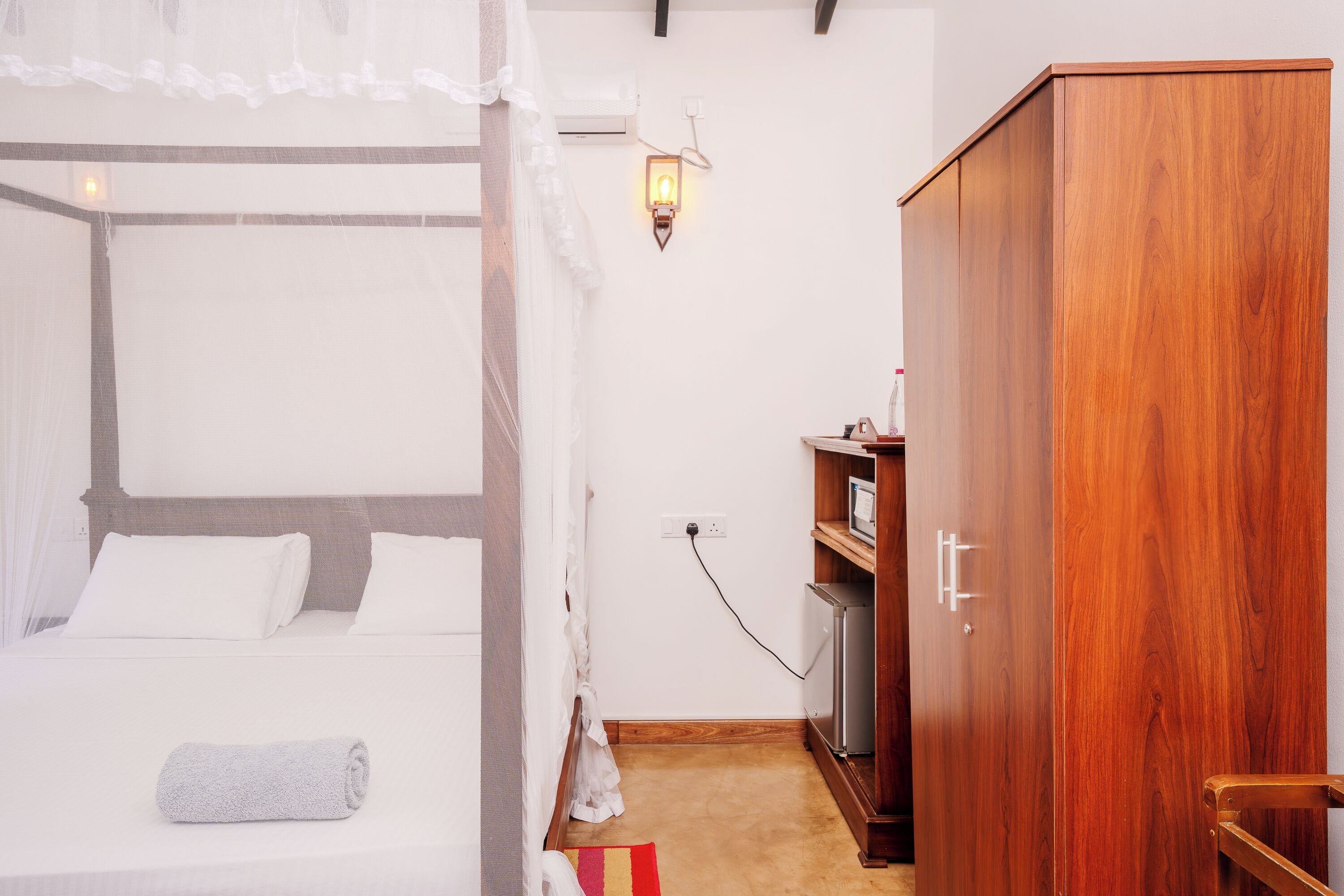 A bedroom with a bed, a wardrobe, a bedside table, a lamp, and a power outlet.