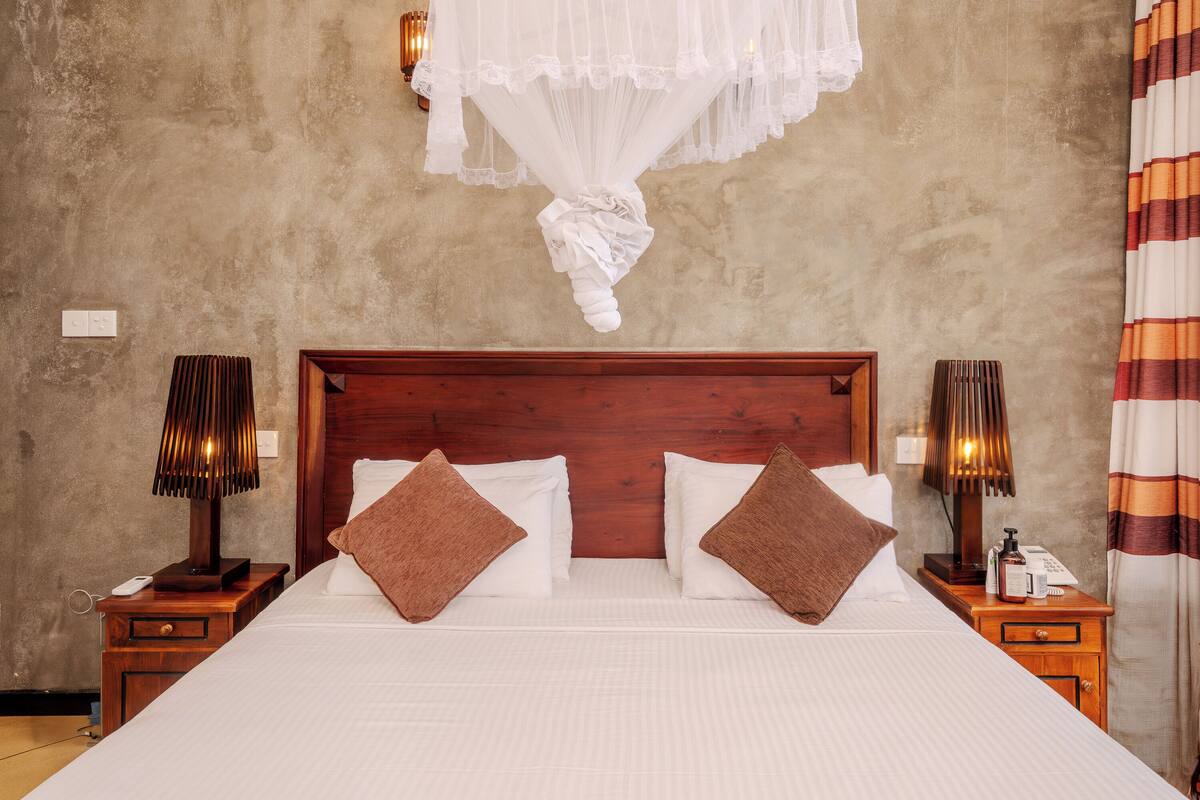 A neatly made bed with a wooden headboard, two bedside lamps, and a bedside table with a phone and toiletries.