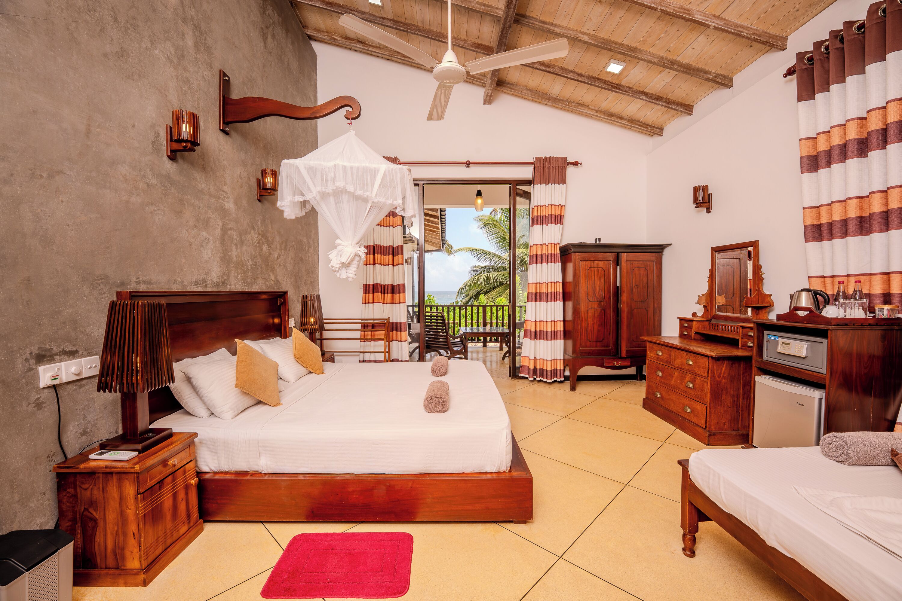A spacious bedroom with a large bed, wooden furniture, a ceiling fan, and a view of the outdoors.