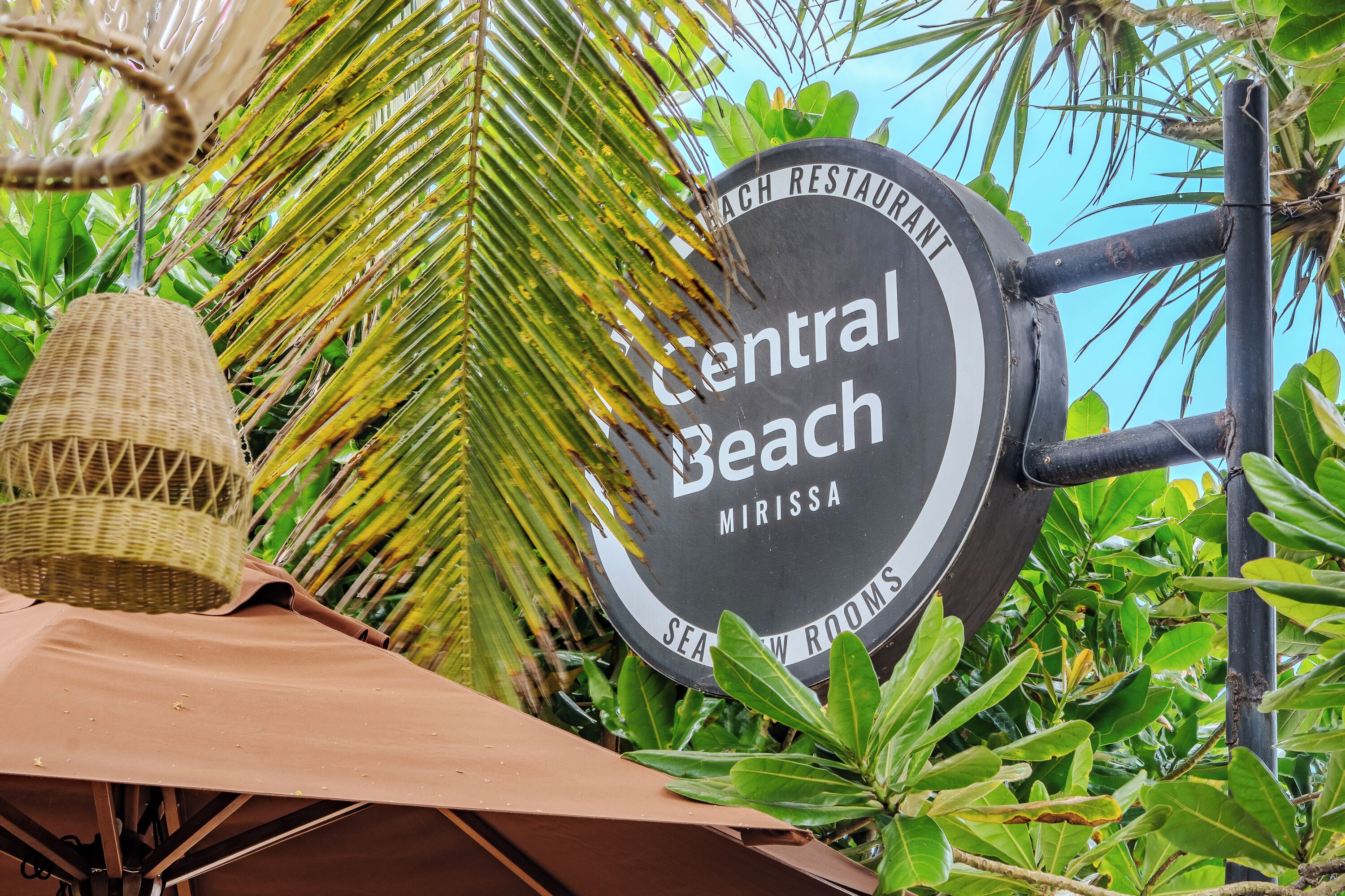 Une enseigne pour le restaurant Central Beach, avec vue sur une végétation luxuriante et un panier suspendu.