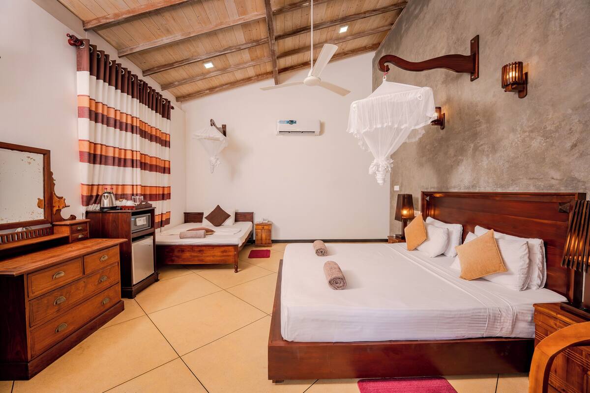 A hotel room with a wooden bed, a wooden dresser, a ceiling fan, an air conditioning unit, and a mosquito net.