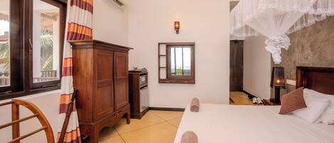 A hotel room with a bed, a wooden wardrobe, a window with curtains, and a nightstand with a lamp.
