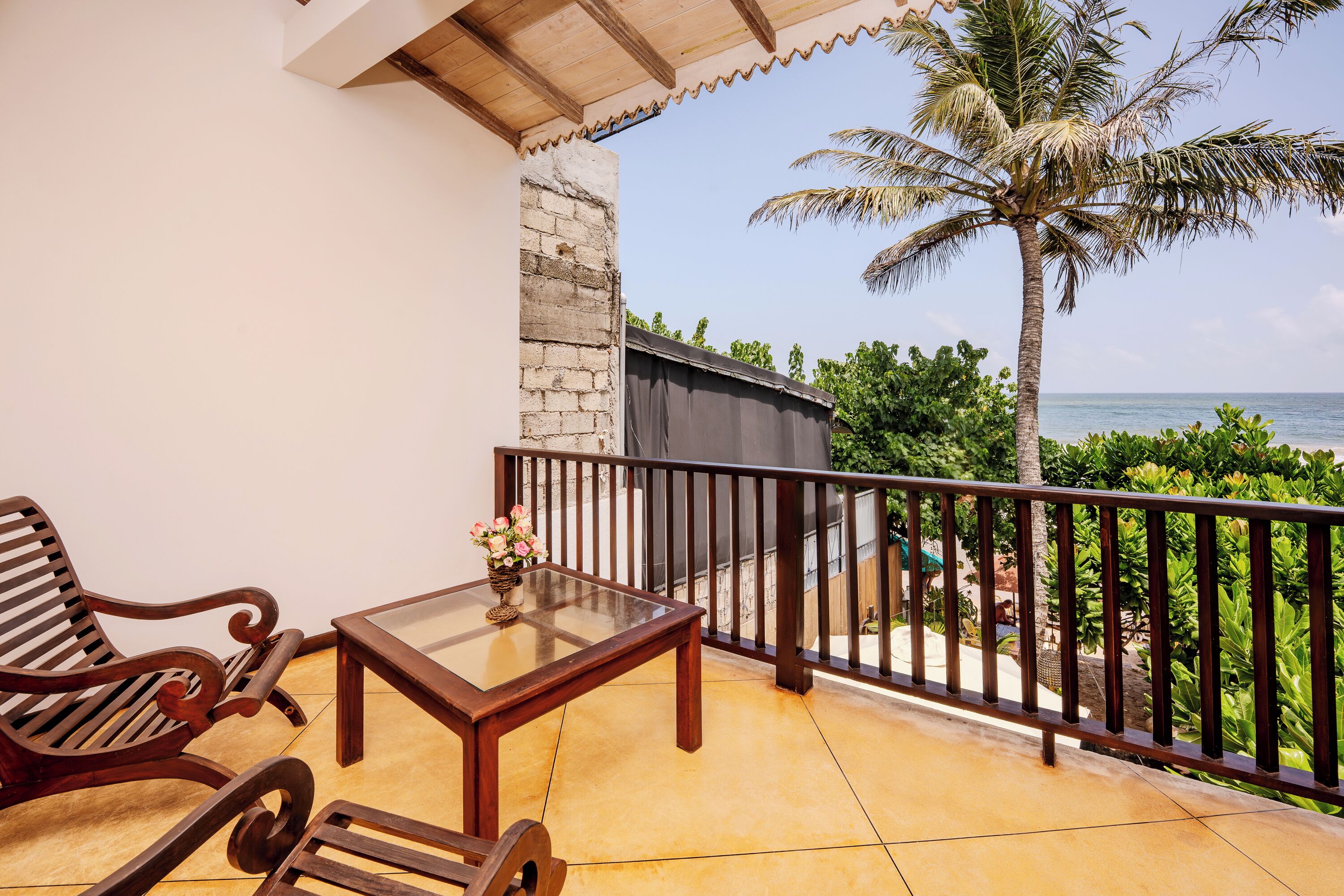 A balcony with a wooden table and chairs, a view of the ocean, and a palm tree.
