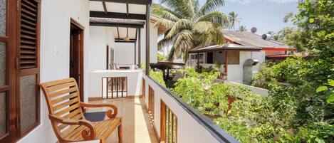 A balcony with a wooden bench and table, overlooking a lush garden and neighboring houses.