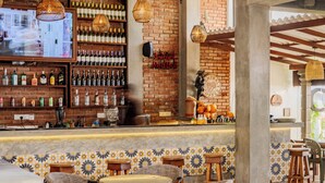 A bar area with a brick wall, shelves of bottles, wicker chairs, and a television screen. - Central Beach Inn (Mirissa)
