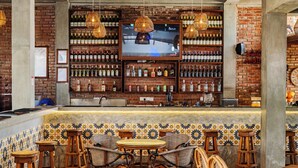 A bar area with a television screen, shelves of bottles, wicker chairs, and a tiled backsplash. - Central Beach Inn (Mirissa)