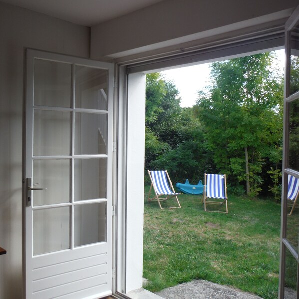 Vista a través de un ventanal a un patio trasero con dos sillas de jardín a rayas y una piscina infantil azul.