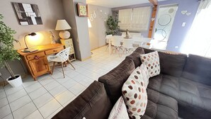 Ein Wohnzimmer mit braunem Ledersofa, einem Holztisch mit Stuhl, einem Esstisch mit Stühlen und einem Blumentopf.