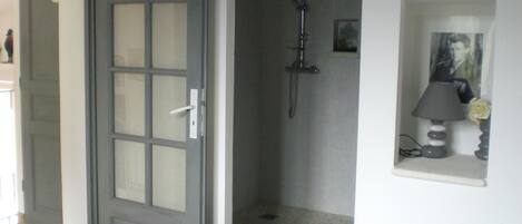 Un baño con ducha, una puerta con paneles de vidrio esmerilado y un pequeño estante con una lámpara y un cuadro enmarcado.