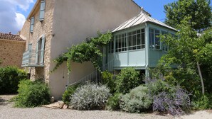 Un bâtiment doté d’une façade en pierre, d’une véranda aux murs de verre et entouré de verdure.