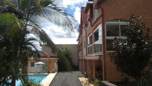 A hotel with a pool, palm trees, and a gravel pathway leading to the entrance. - apartment rental Le Tampon (Réunion) (LE TAMPON)