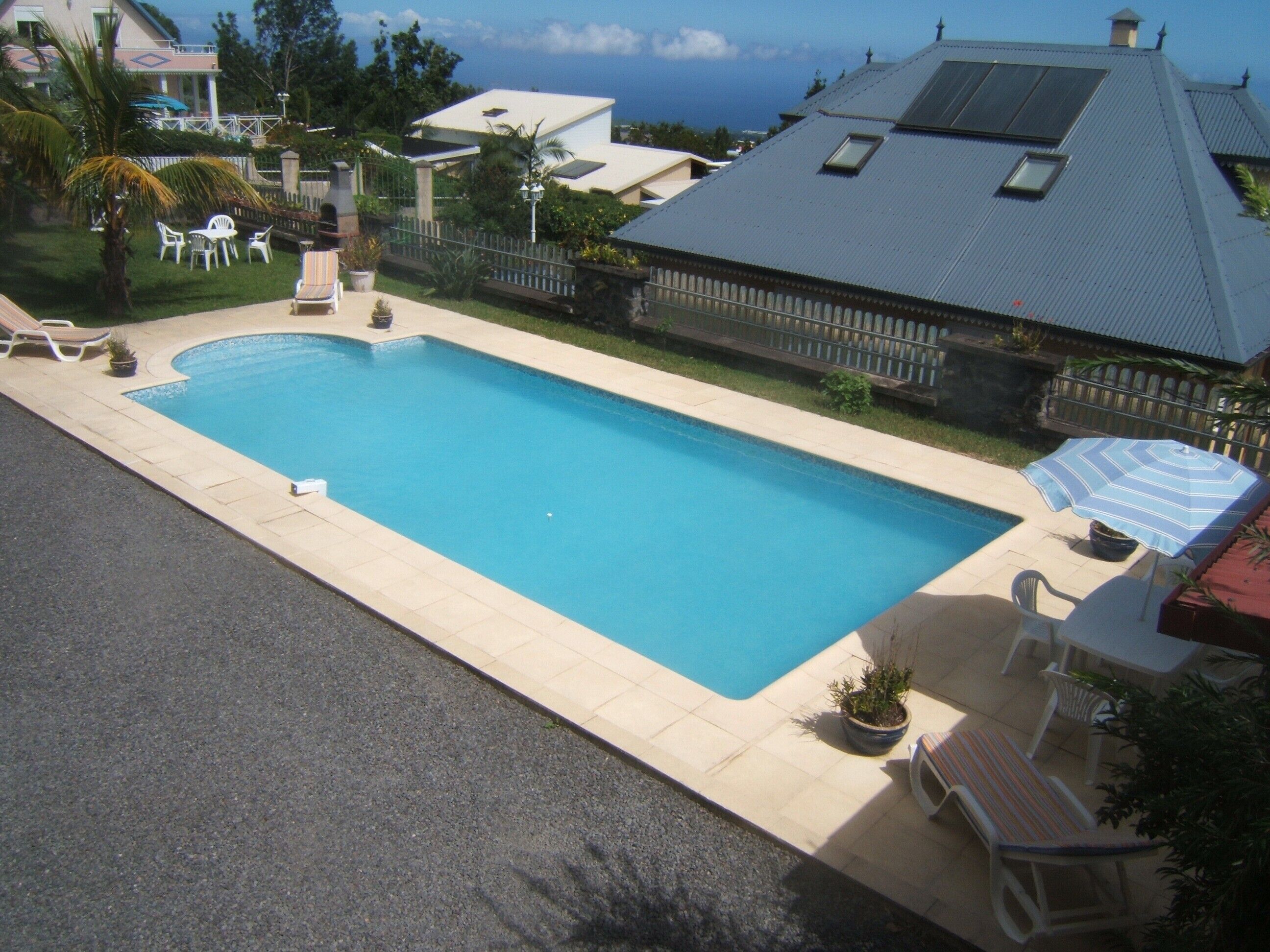Une piscine rectangulaire avec une terrasse carrelée, entourée d’une clôture et agrémentée de plantes en pot.