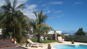 A pool area with lounge chairs, a barbecue grill, and palm trees. - apartment rental Le Tampon (Réunion) (LE TAMPON)