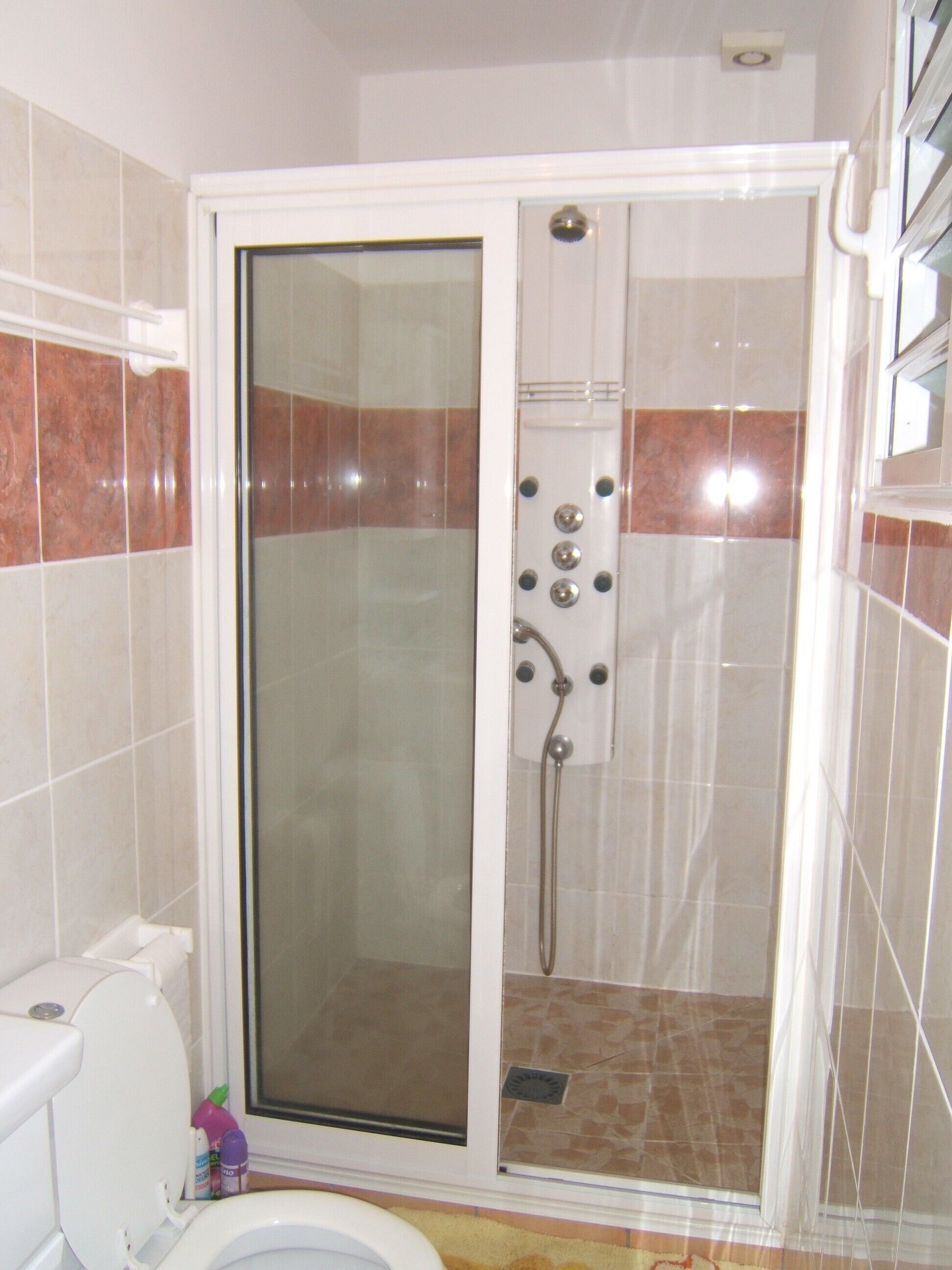 Ein Badezimmer mit einer Duschkabine, einer Toilette und Fliesenboden.