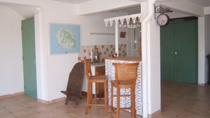 A kitchen with a tiled backsplash, wooden chairs, a small bar area, and a green door. - apartment rental Le Tampon (Réunion) (LE TAMPON)