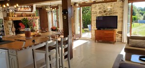A spacious living area with a stone wall, a wooden dining table set for four, a television on a wooden stand, and a sofa. - BEAUTIFUL STONE FARMHOUSE WITH PRIVATE HEATED POOL (Meuzac)