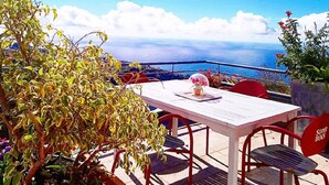 An outdoor patio with a table and chairs, overlooking a scenic view of the sea and distant land. - Amazing views, large terrace and garden. (Madère)