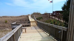 Una pasarela de madera que lleva a una zona de playa con un banco y una bandera.