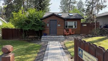 Una casa de madera con un camino de entrada pavimentado, una puerta principal y un pequeño patio con sillas.