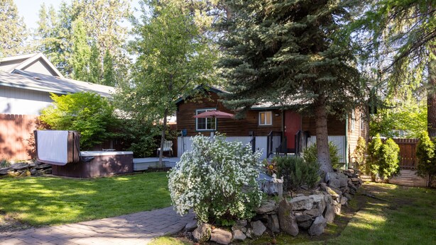 Una casa de madera con un camino de piedra, un jacuzzi y un jardín bien cuidado.