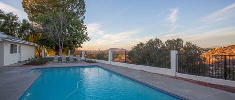 A swimming pool with a curved edge, surrounded by a white fence and a tree.