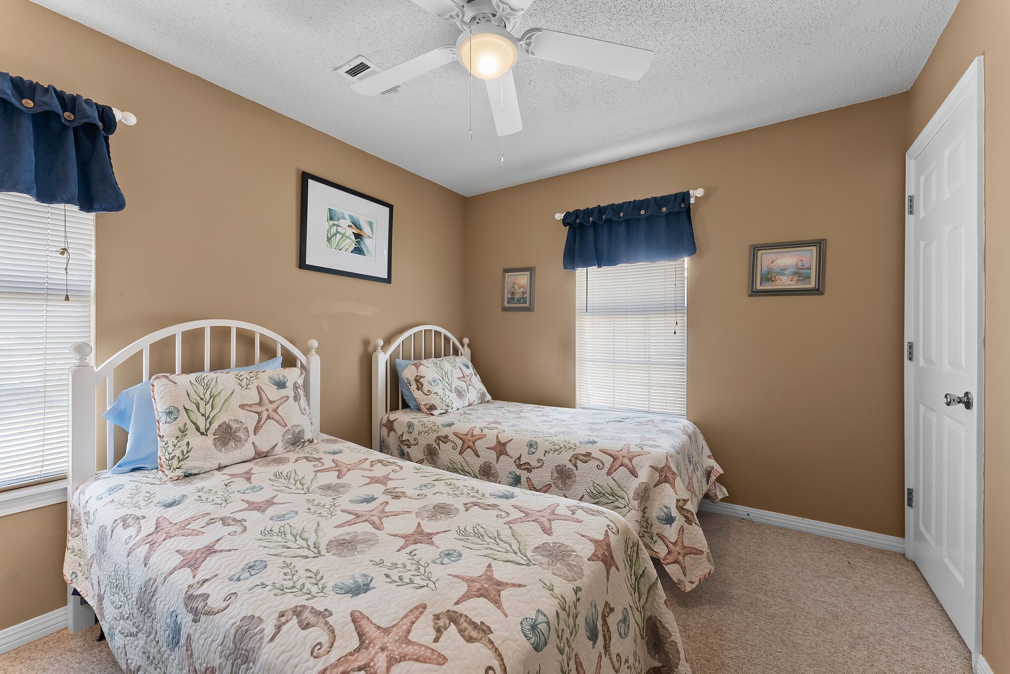A bedroom with two beds, a ceiling fan, and framed pictures on the walls.