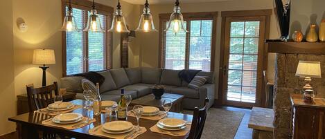 A dining area with a wooden table set for four, a sofa, and a stone fireplace.