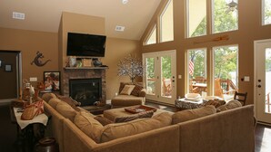 A cozy living room with a fireplace, large windows, and a comfortable seating area. - Private Lakeside, private Dock, Outddor Kitchen Fire Pit & More (Chappells)
