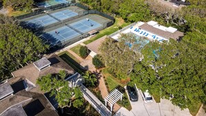 Vista aérea de una propiedad con varias canchas de tenis, una piscina y un estacionamiento.
