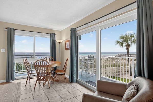 A room with a balcony, a dining table with chairs, and a sofa.