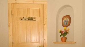 Una puerta de madera con la leyenda 'LAUNDRY', una silla de madera, un estante con una planta en maceta y un cuadro enmarco.