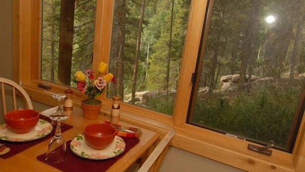 Una mesa de comedor con cuencos rojos y un jarrón de flores, con vista a un bosque.