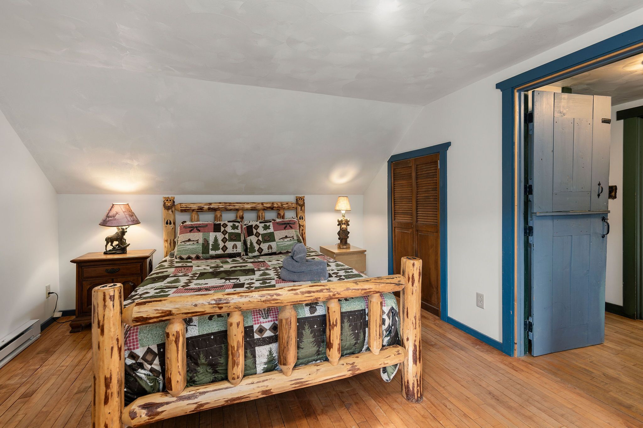 A bedroom with a wooden bed, two bedside tables with lamps, a wardrobe, and a door leading to another room.