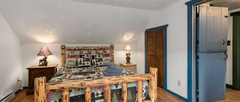 A bedroom with a wooden bed, two bedside tables with lamps, a wardrobe, and a door leading to another room.