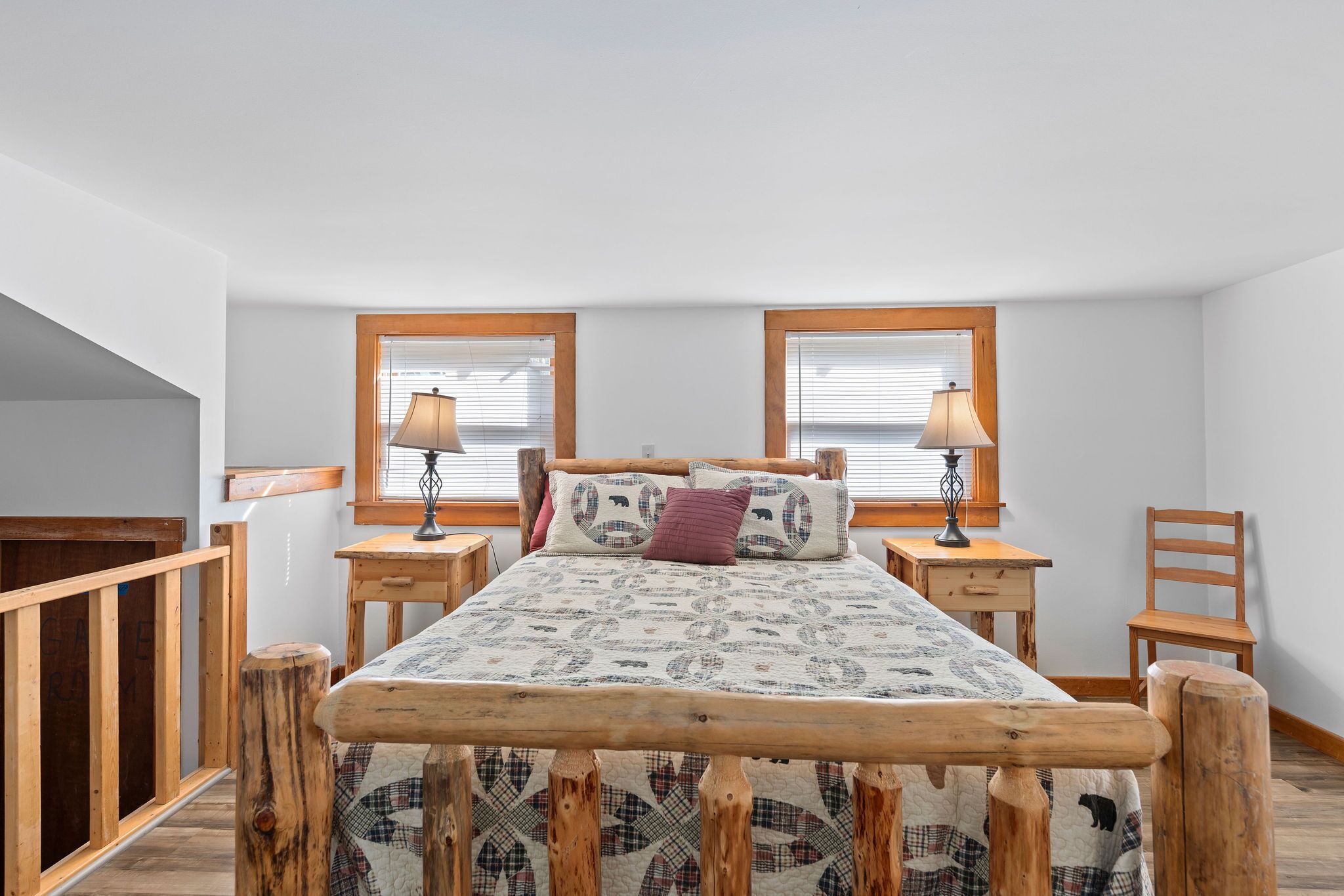 Une chambre à coucher avec un lit en bois, deux tables de chevet avec des lampes, une chaise et une fenêtre avec des stores.