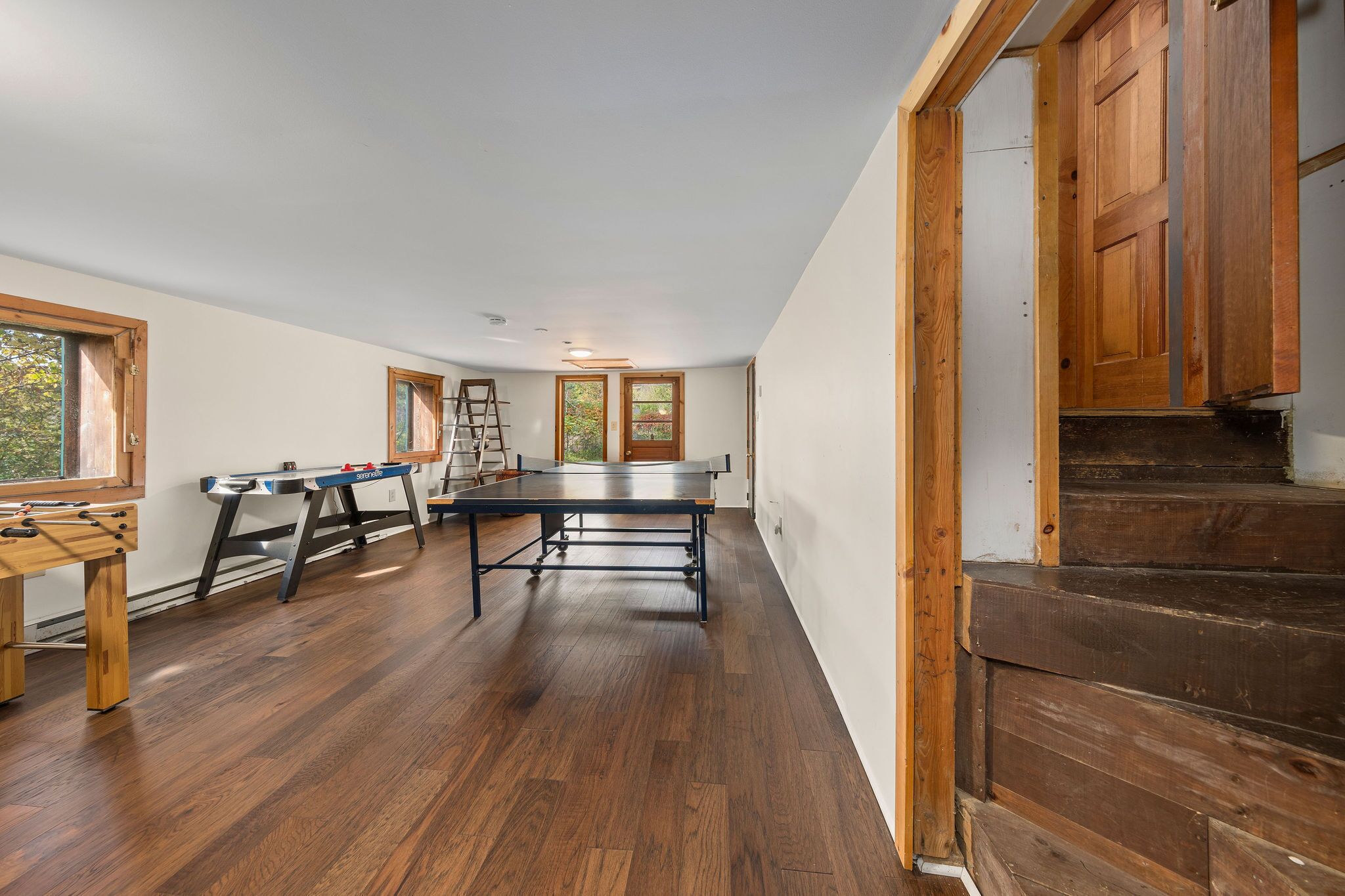 A spacious room with hardwood floors, a ping pong table, a foosball table, and a staircase leading to an upper level.