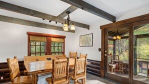 A wooden dining table with chairs, a large window with blinds, a map on the wall, and a door leading to an outdoor deck. - Secluded Family Getaway Cabin near Whiteface (Upper Jay)