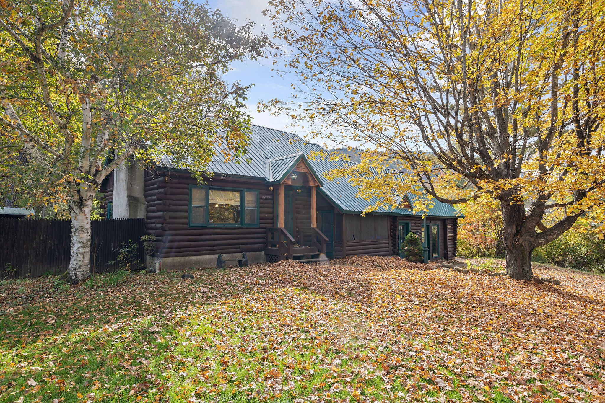 A rustic log cabin with a metal roof, surrounded by trees with autumn leaves.