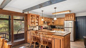 A spacious kitchen with wooden cabinets, a large island with seating, and a view through the glass door. - Secluded Family Getaway Cabin near Whiteface (Upper Jay)