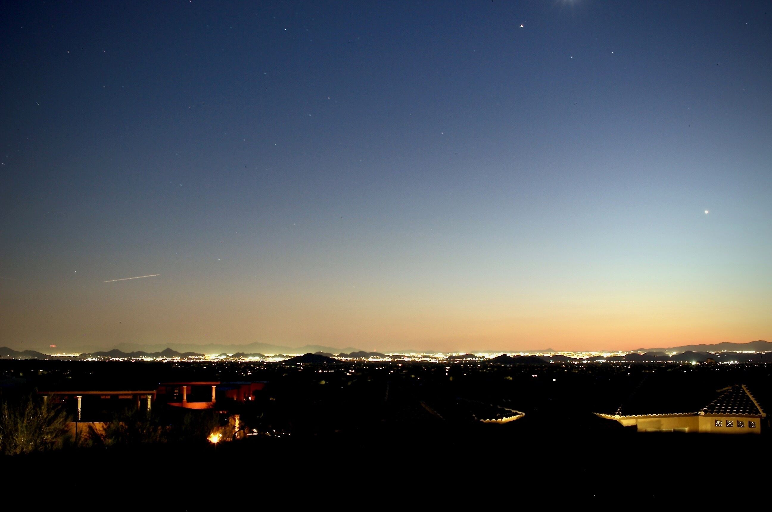 A nighttime view of a cityscape with distant mountains, a clear sky, and a few visible stars.