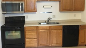 A kitchen with wooden cabinets, a stainless steel microwave, a black stove, a sink, and a dishwasher. - Coastal Cottage near beaches, dining & shopping! (Naples)