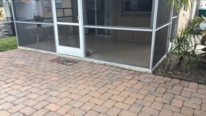 A covered patio area with a brick floor and a sliding glass door leading to an interior space. - Coastal Cottage near beaches, dining & shopping! (Naples)