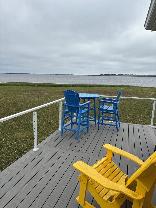A deck with blue and yellow Adirondack chairs, a small table, and a view of a body of water. - Ocean Edge Beach House (Malpeque)