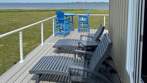 A deck with two blue chairs and a table, overlooking a grassy area and a body of water. - Ocean Edge Beach House (Malpeque)